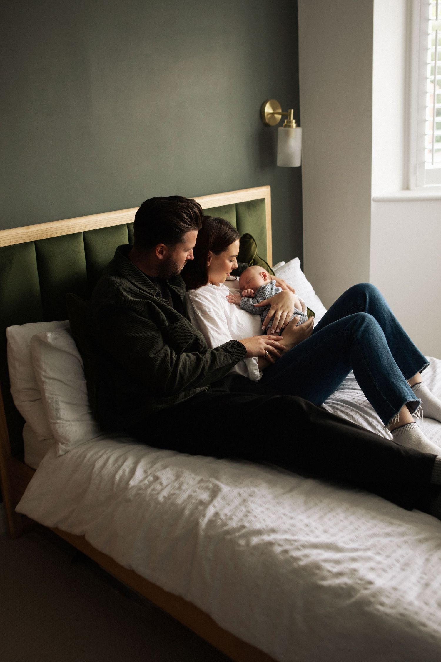 New parents relaxing on bed with newborn baby in cozy bedroom.