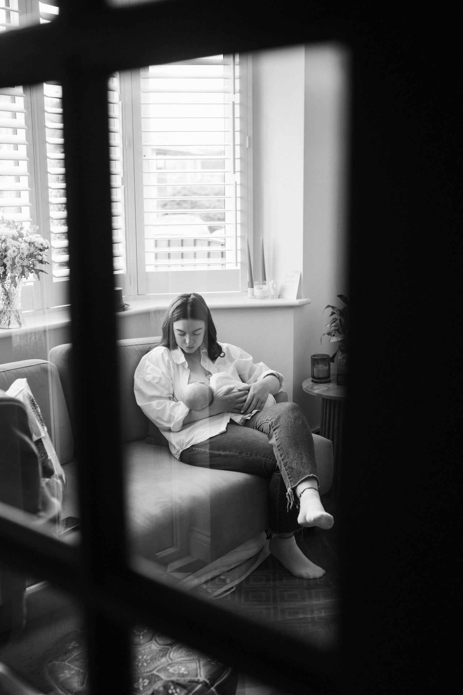 Black and white photo of a mother breastfeeding her newborn baby while seated by a window.