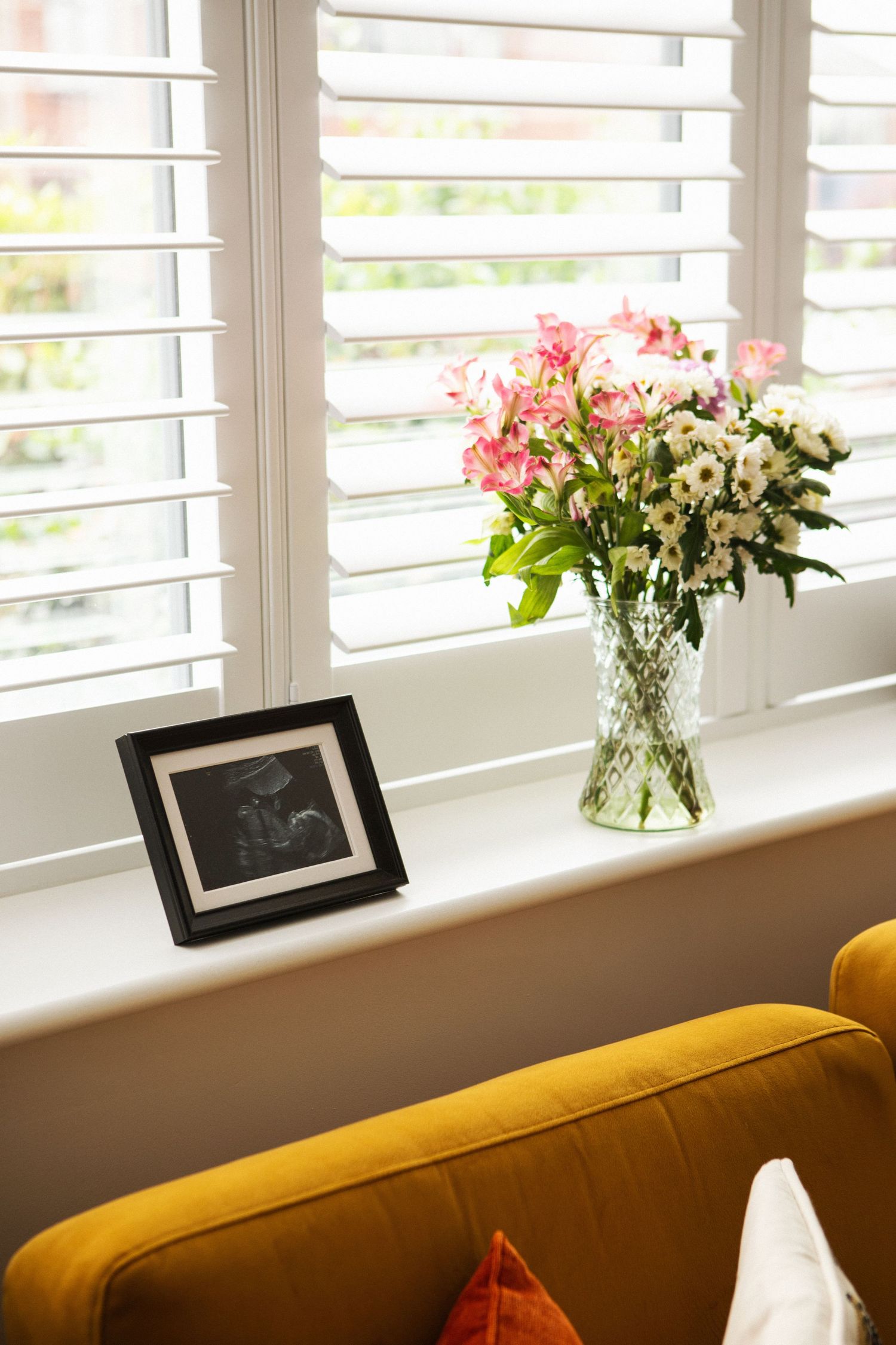Framed ultrasound photo beside a vase of pink and white flowers on a sunny windowsill.