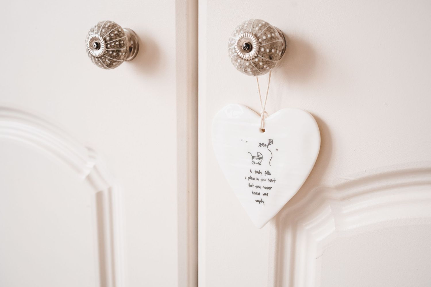 White ceramic heart keepsake hanging on cream wardrobe door handles.