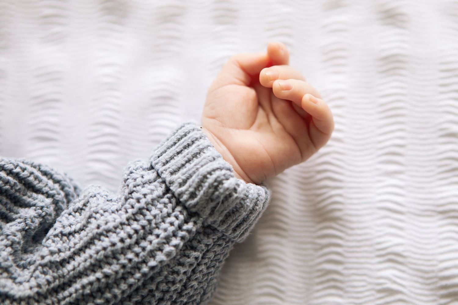 Close-up of a newborn baby's tiny hand and fingers wearing a grey knit sweater sleeve.