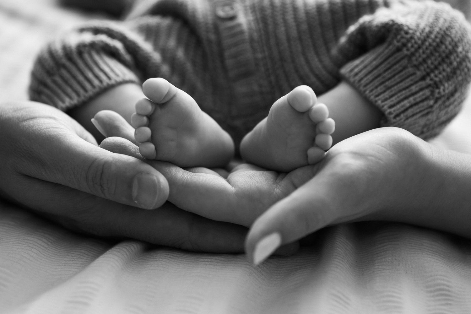 Black and white photo of parents cradling tiny newborn baby feet in their hands.