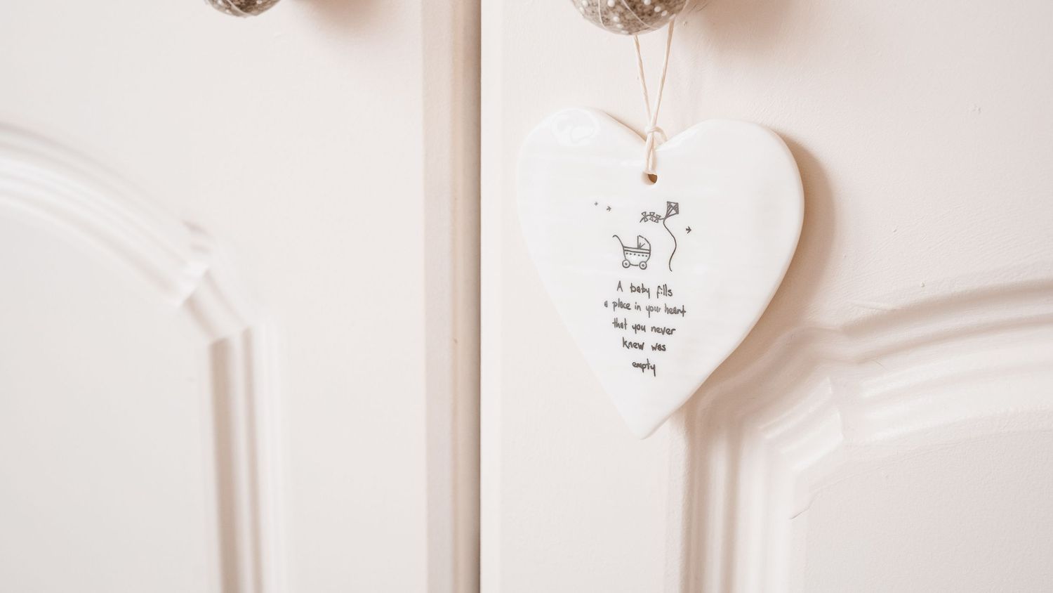 White ceramic heart-shaped keepsake plaque with illustration hanging on cream painted wooden door.