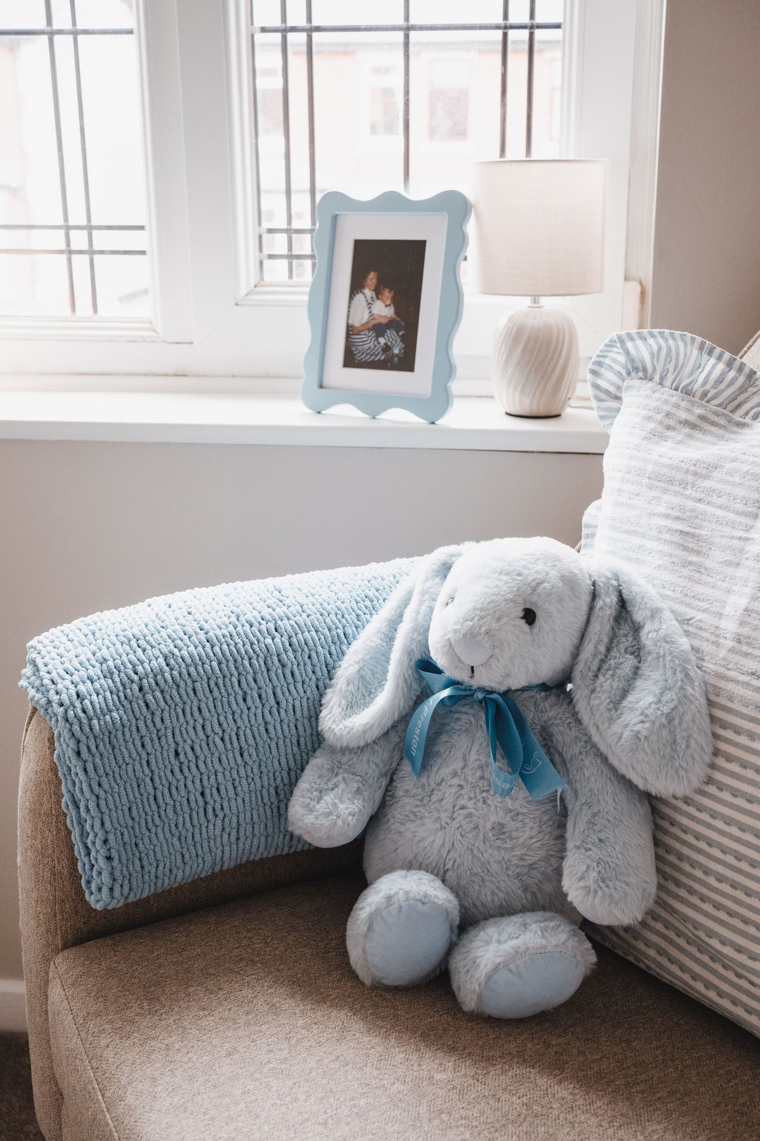 Blue bunny soft toy with blue blanket beside framed photo on chair.