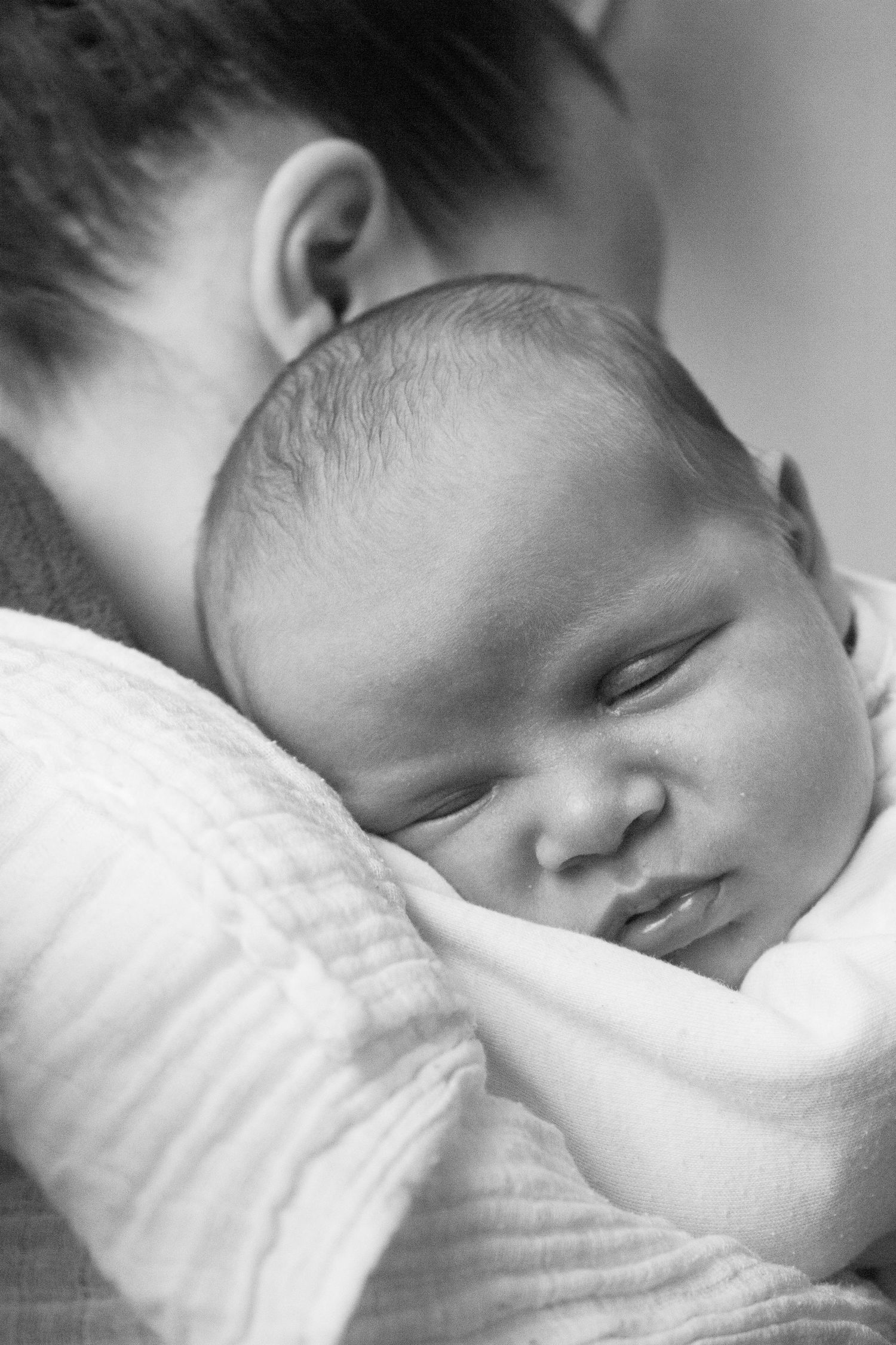 Black and white close-up of a sleeping newborn baby resting on a parents shoulder.