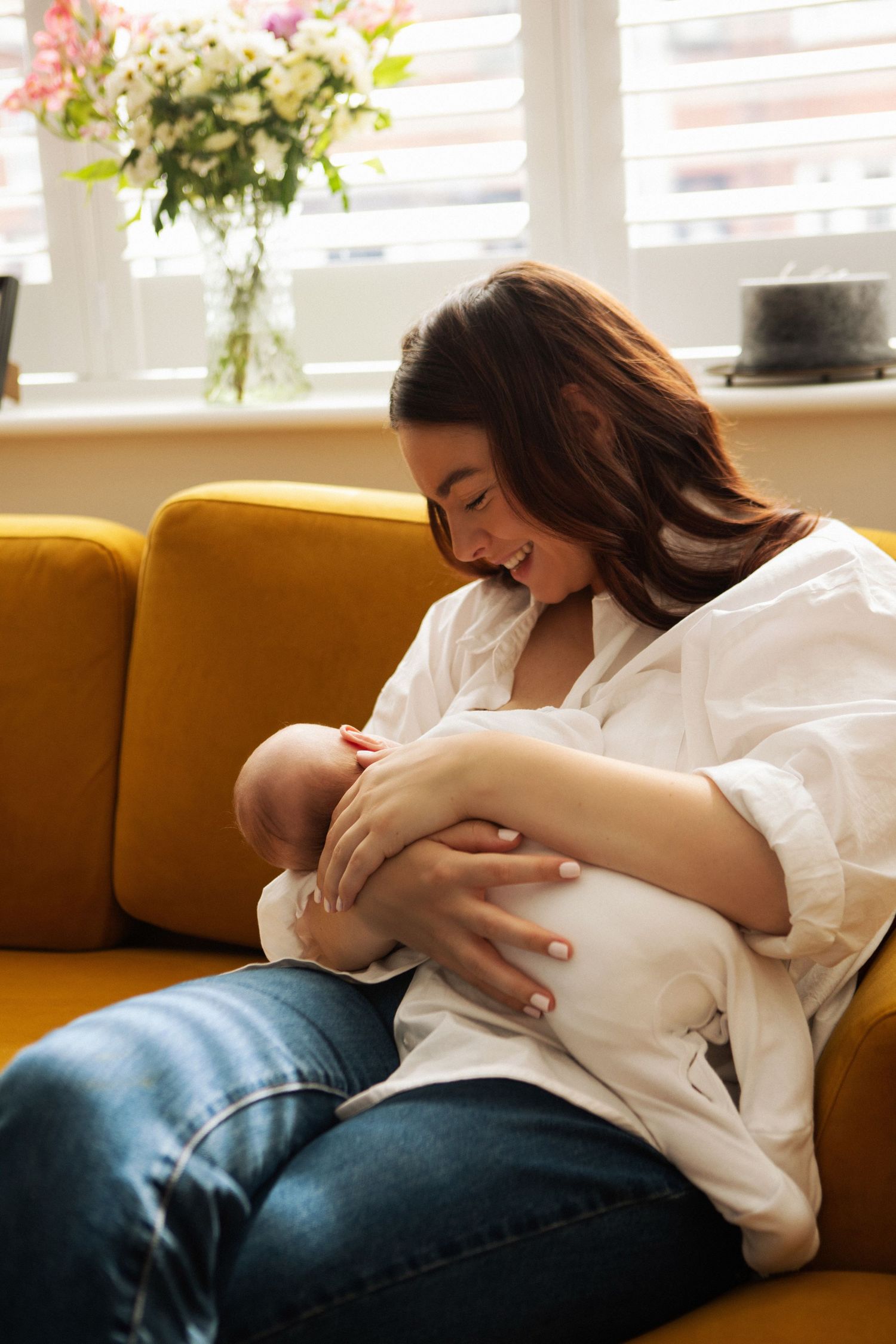 Happy mother breastfeeding newborn baby on yellow sofa at home.