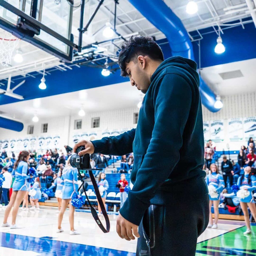 Sports photographer standing on the sideline holding a professional camera during a basketball game.
