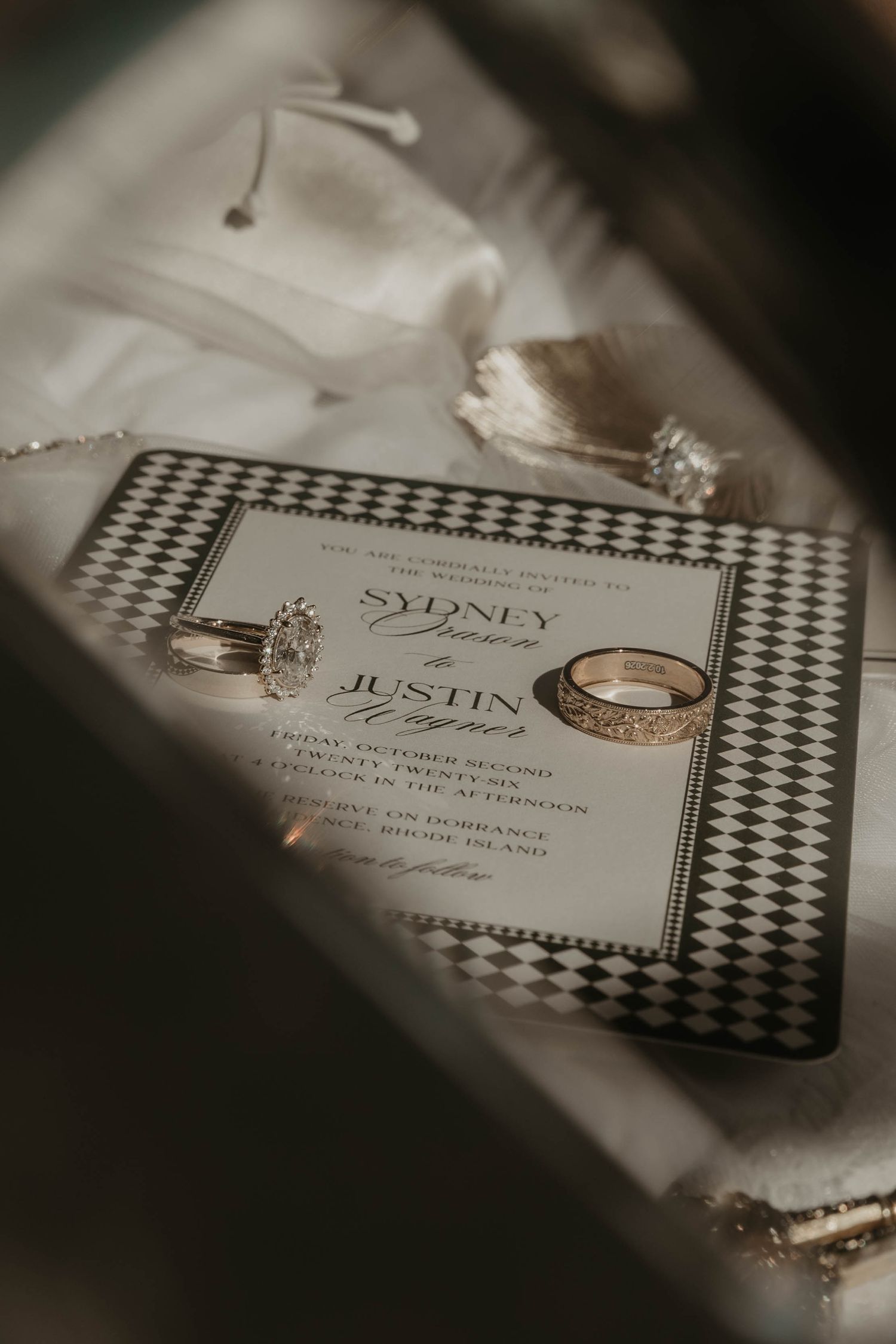 Elegant wedding invitation for Sydney and Justin with diamond pattern border, accompanied by sparkling engagement and wedding rings.