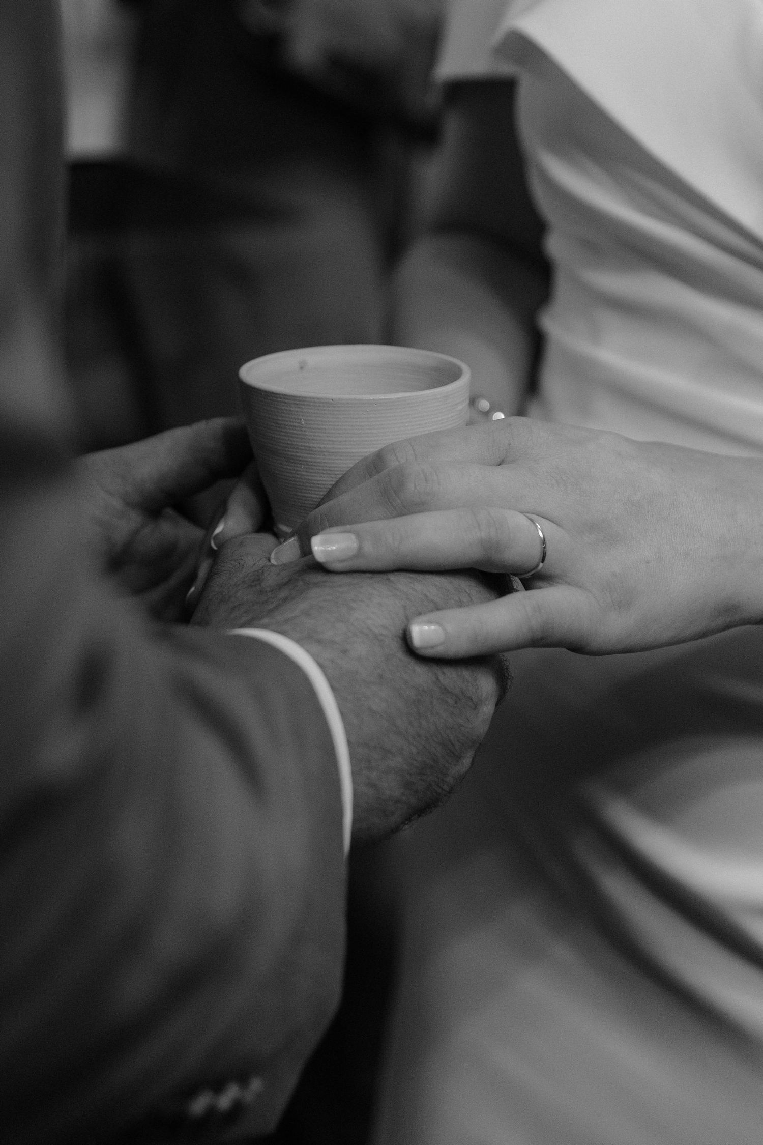 Black and white photo of a couple holding a small cup together, wearing wedding rings, symbolizing a marriage ceremony.