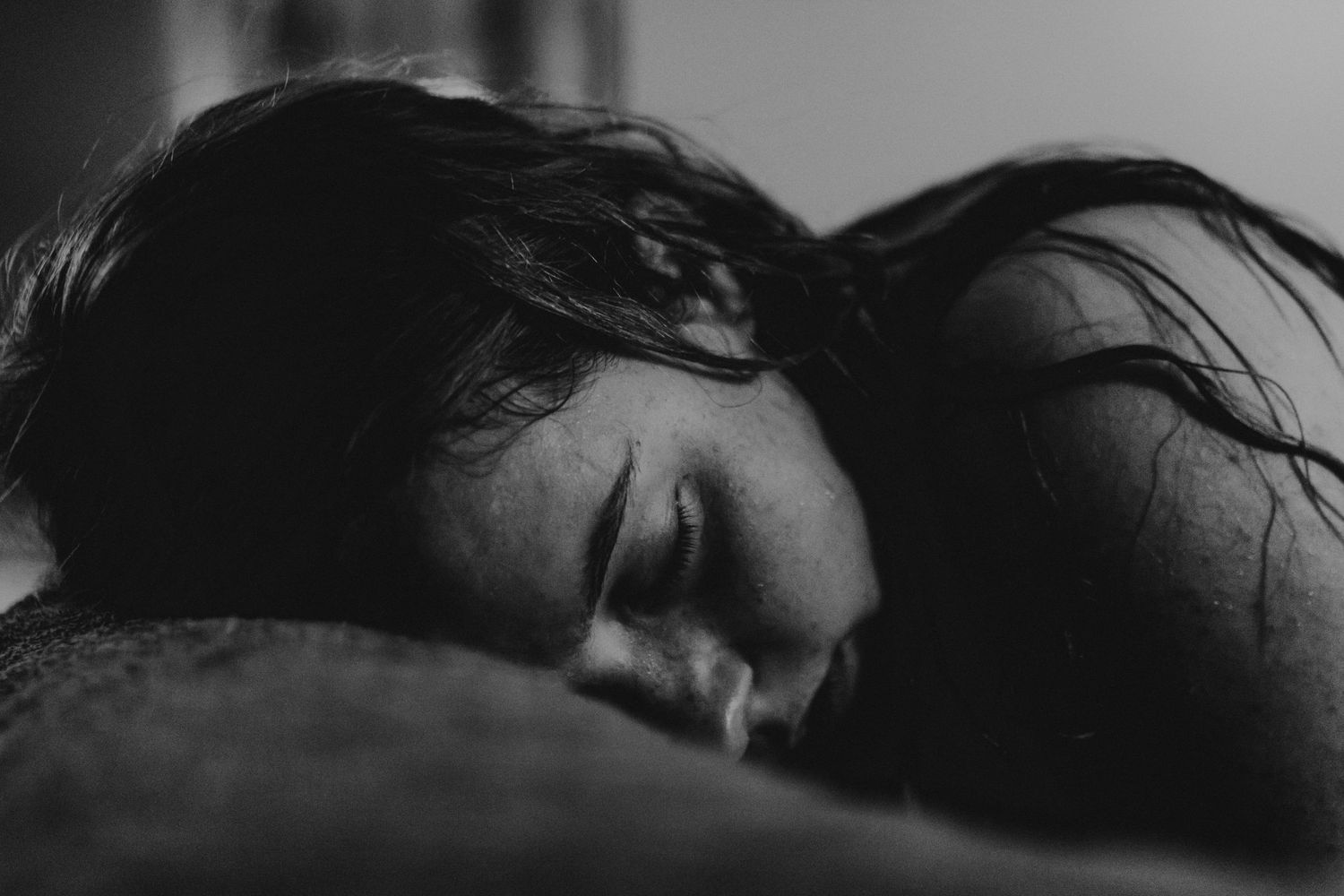 A woman rests peacefully with her eyes closed in a moody black and white close-up portrait. top rated RI birth photographer