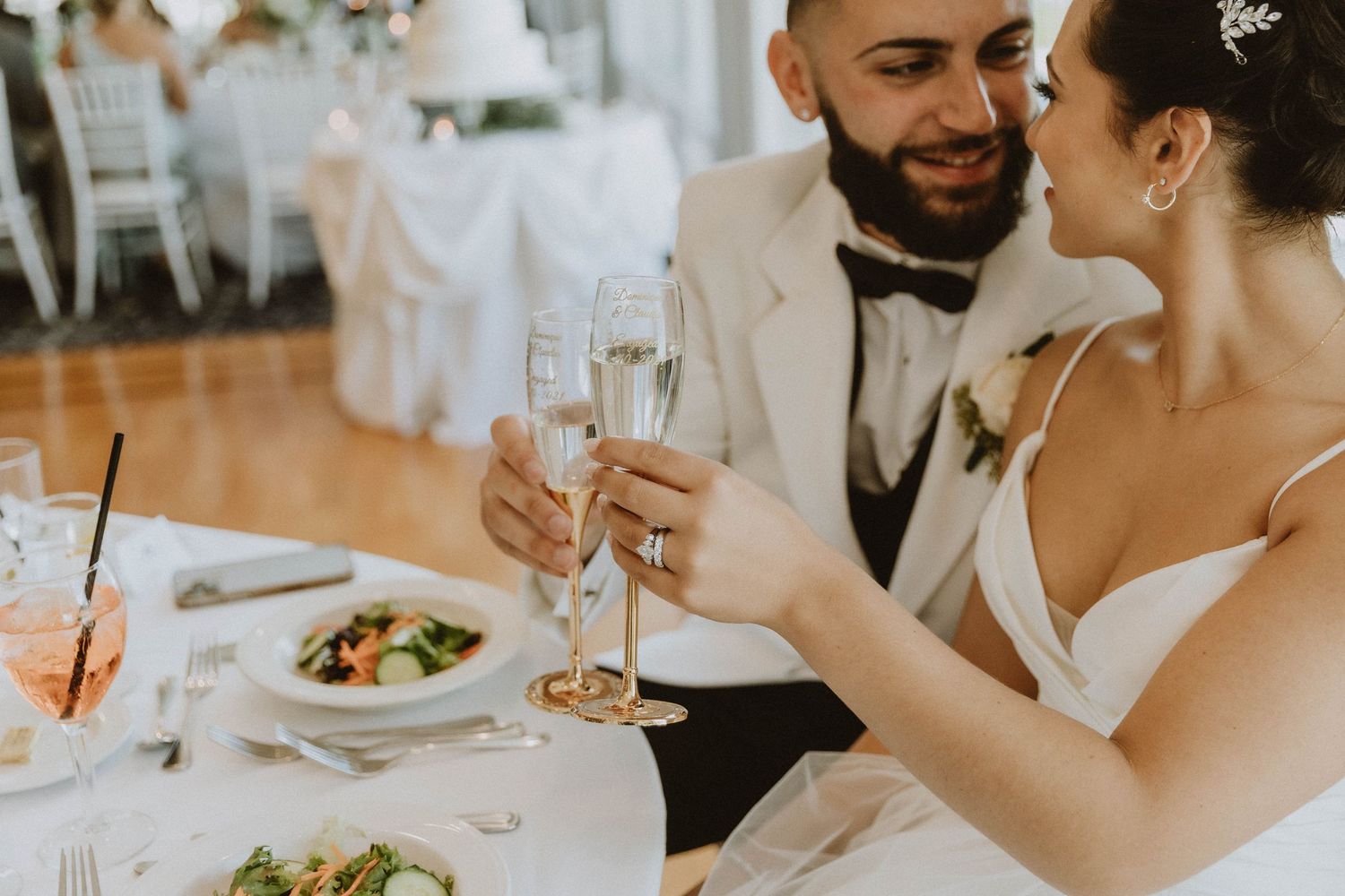Bride and groom toasting with champagne glasses at wedding reception dinner table.