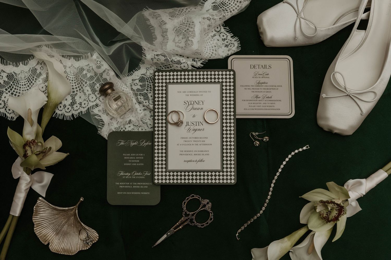 Elegant wedding flat lay with houndstooth invitation suite, white ballet flats, pearl bracelet, and white orchids on green velvet.