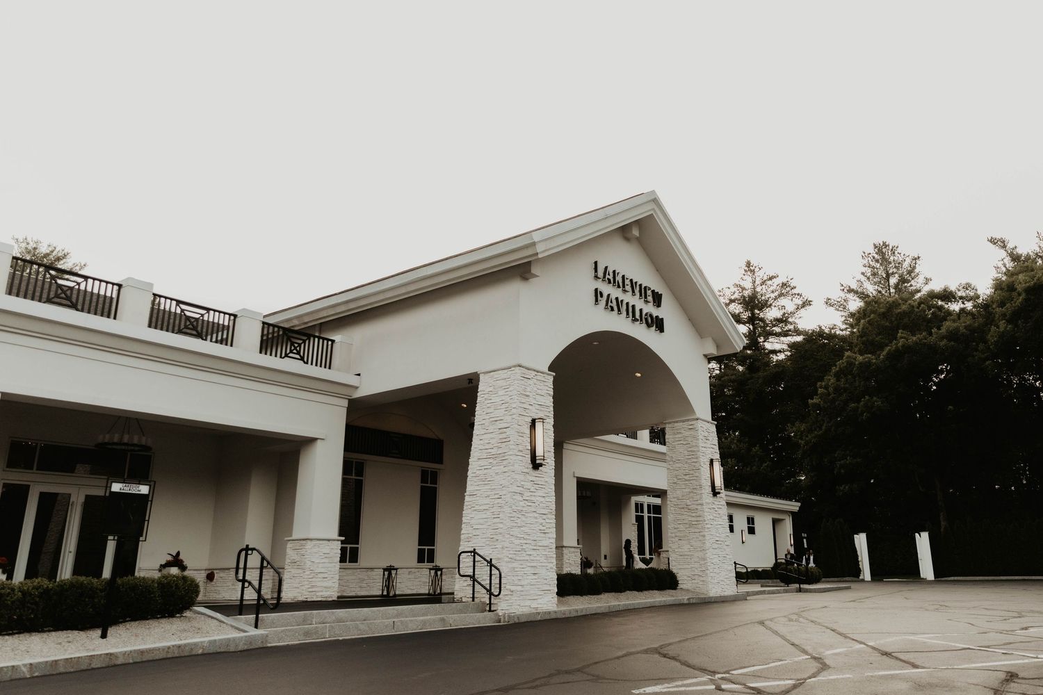 Laketon Pavilion event venue exterior featuring white facade, stone accents, covered entrance, and lush trees on overcast day.
