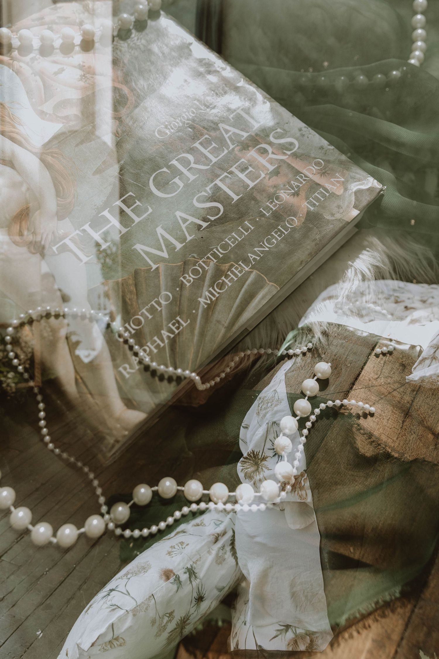 A book titled The Great Masters rests among pearl necklaces and soft fabrics in a vintage aesthetic flat lay.