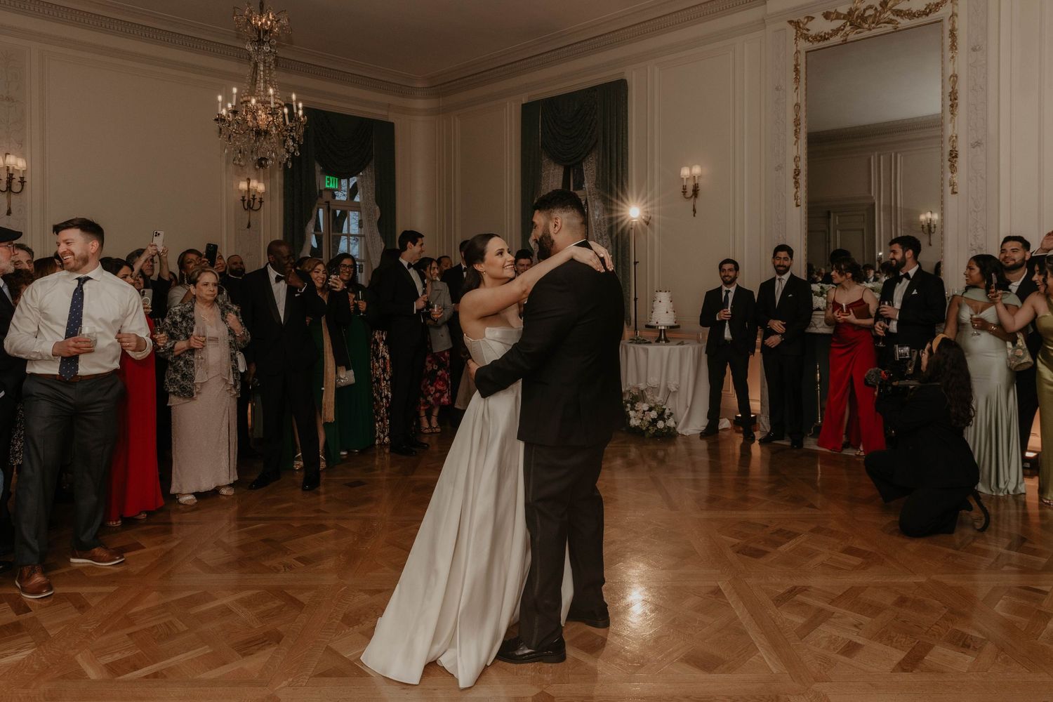 Bride and groom share their first dance at elegant wedding reception while guests watch in grand ballroom.