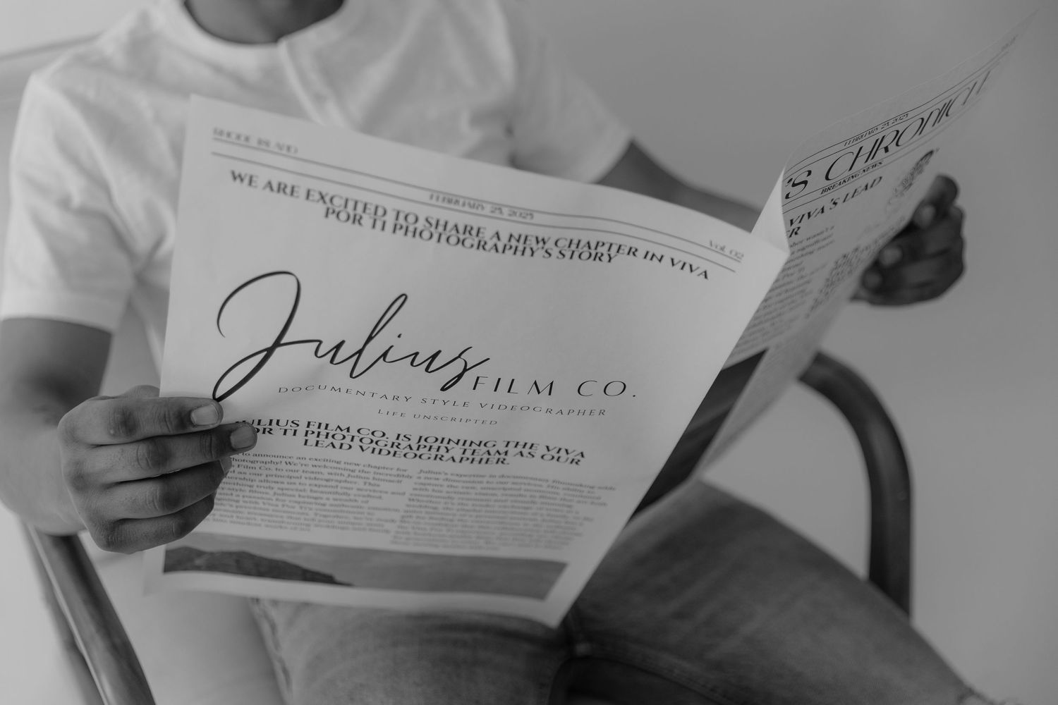 Man in white t-shirt reading Julius Film Co newspaper magazine in black and white photo.