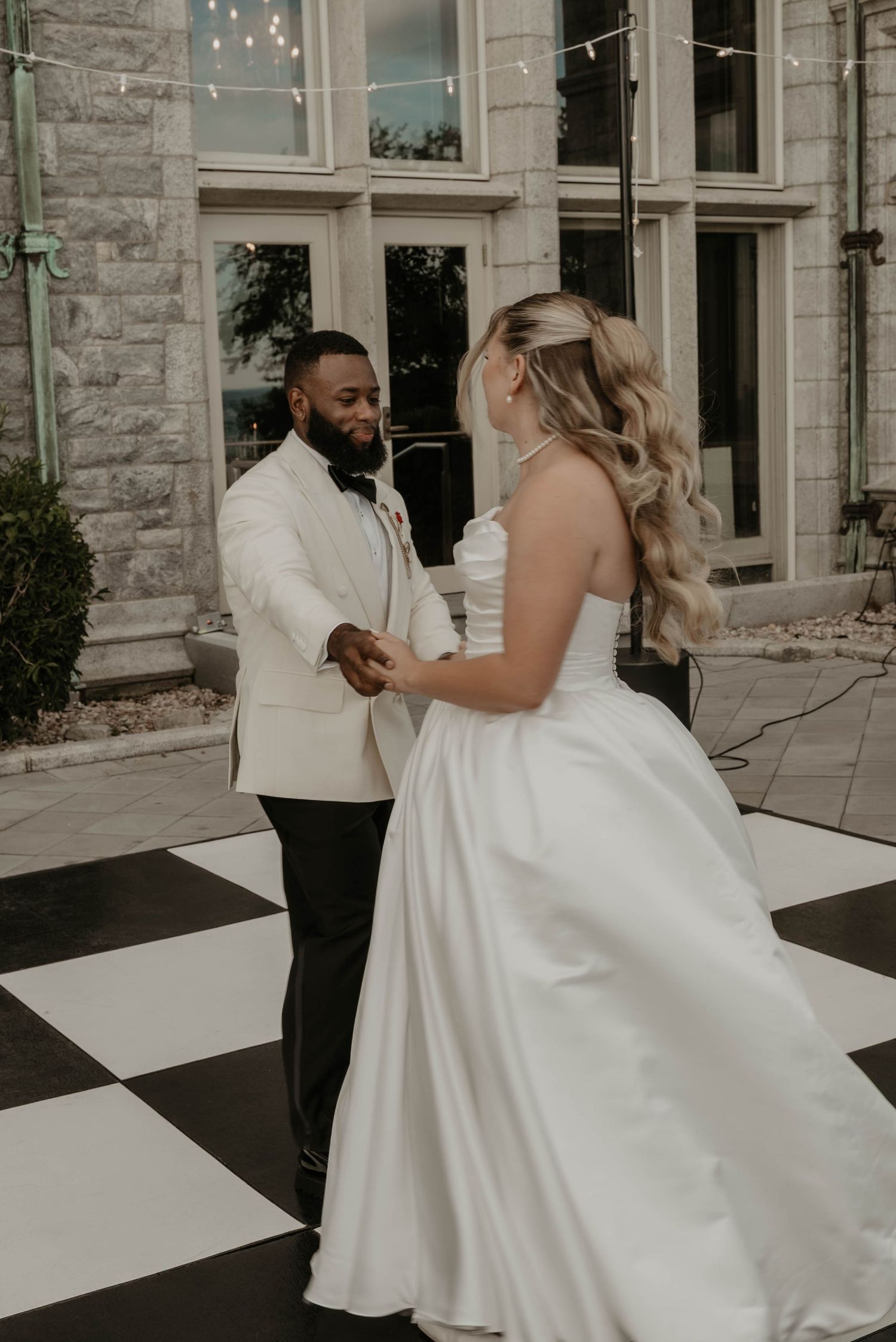 Bride and groom share first dance on black and white checkered floor at elegant stone venue.