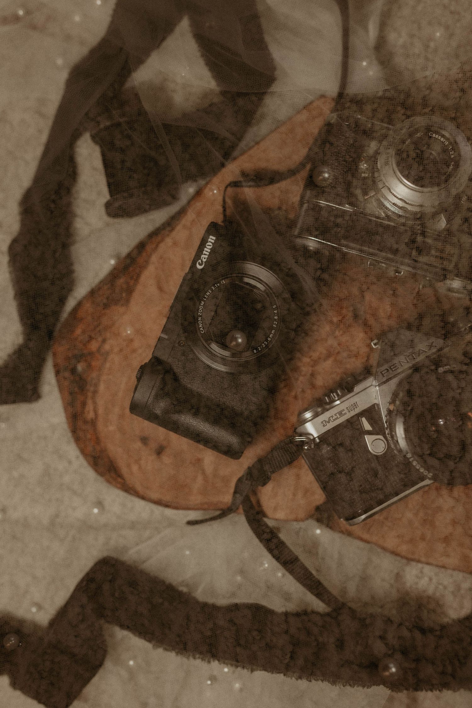 Vintage Canon and retro film cameras arranged on a brown leather bag with a textured blanket backdrop.