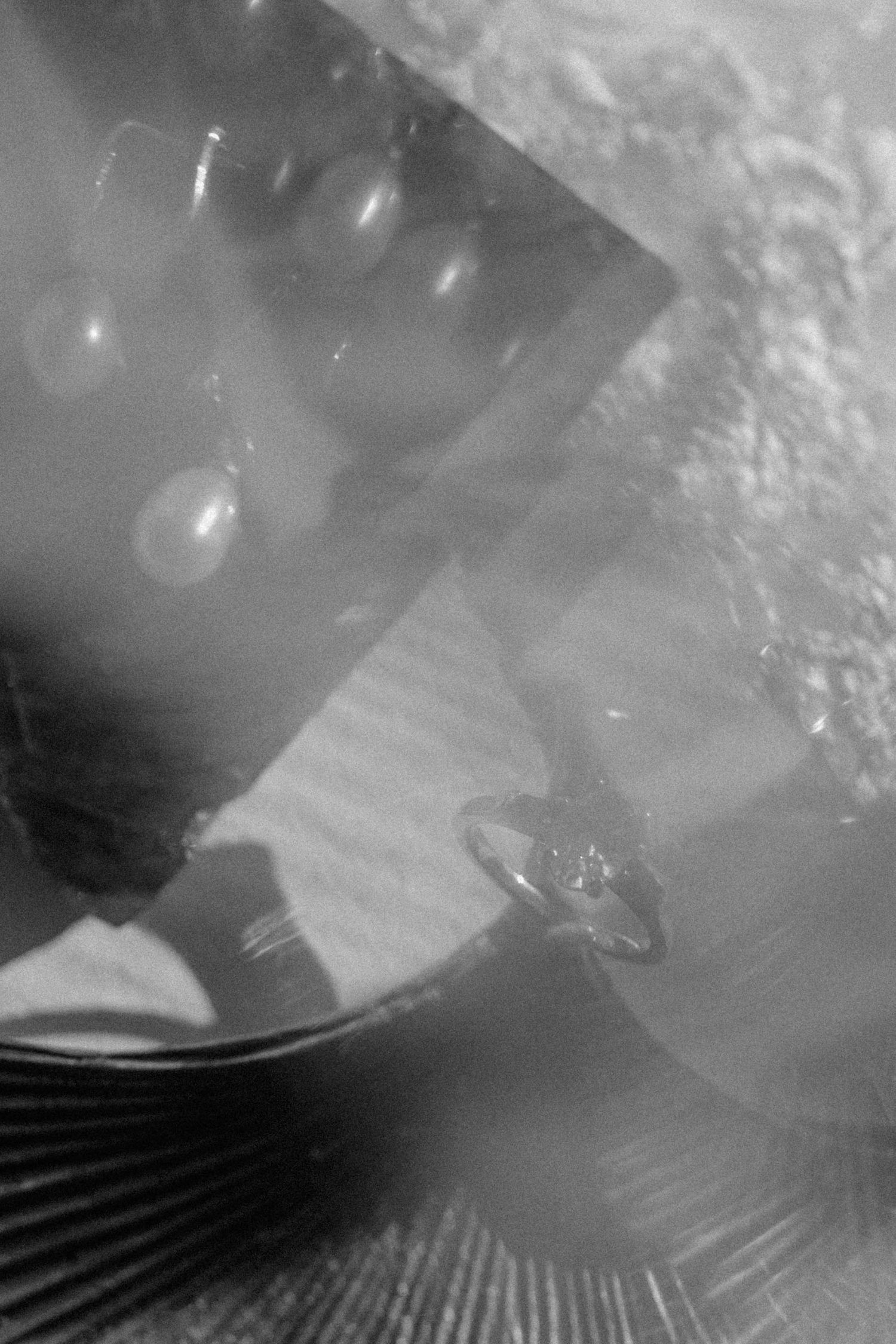 Black and white photo of pearl drop earrings and a diamond ring displayed on a reflective surface.