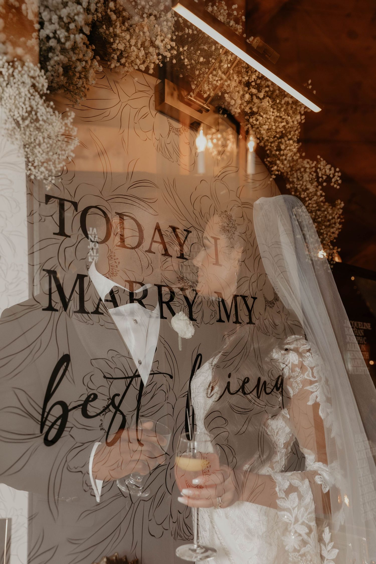 Bride and groom kissing behind a wedding sign reading Today I Marry My Best Friend, adorned with white floral decor.