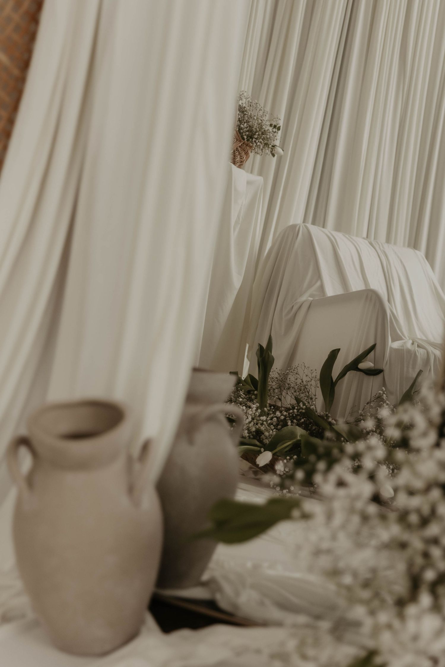 Elegant white draped fabric backdrop with ceramic vase and delicate baby's breath flowers in a soft neutral wedding decor setting.