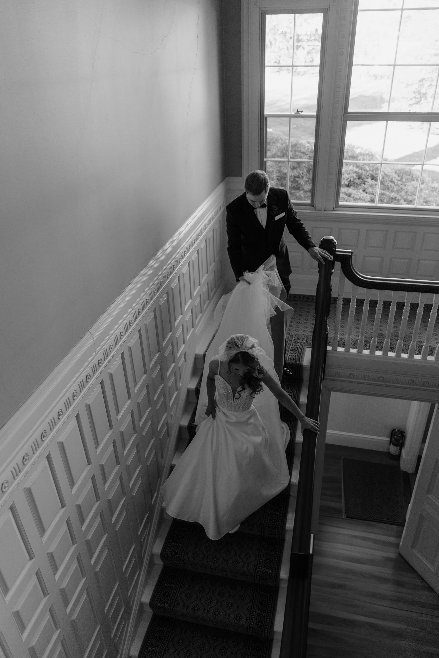 Black and white photo of bride and groom descending elegant staircase, captured from above on their wedding day.