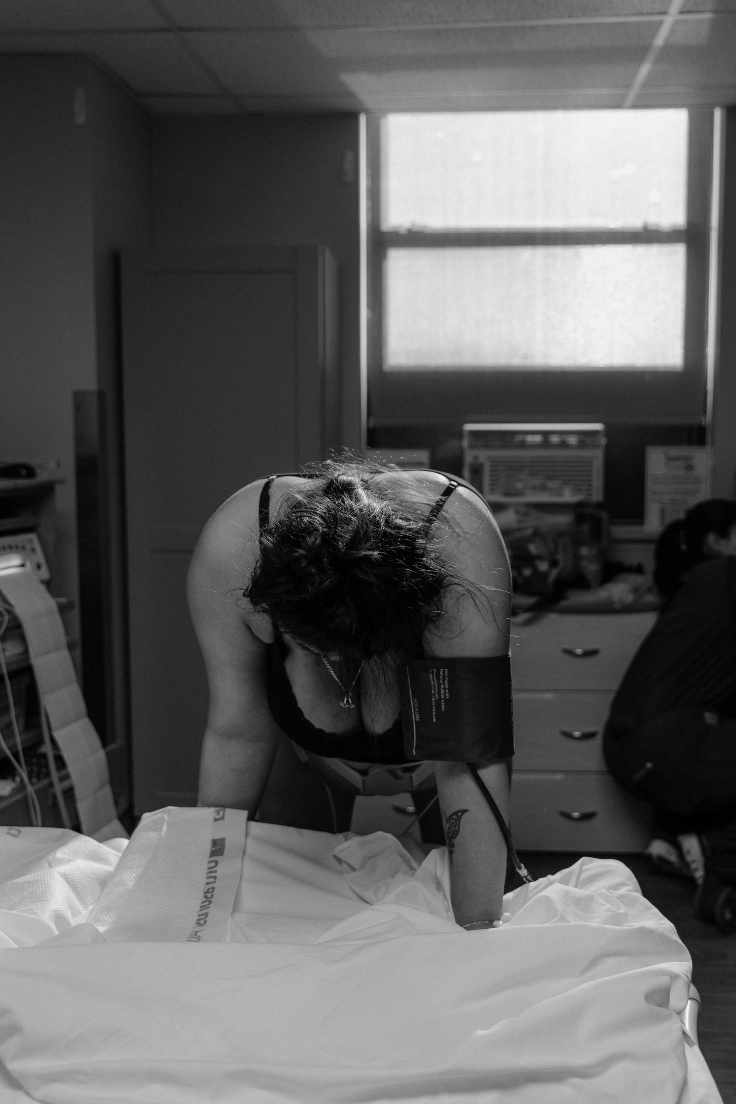 Black and white photo of a woman leaning over a hospital bed during labor, in a medical room.