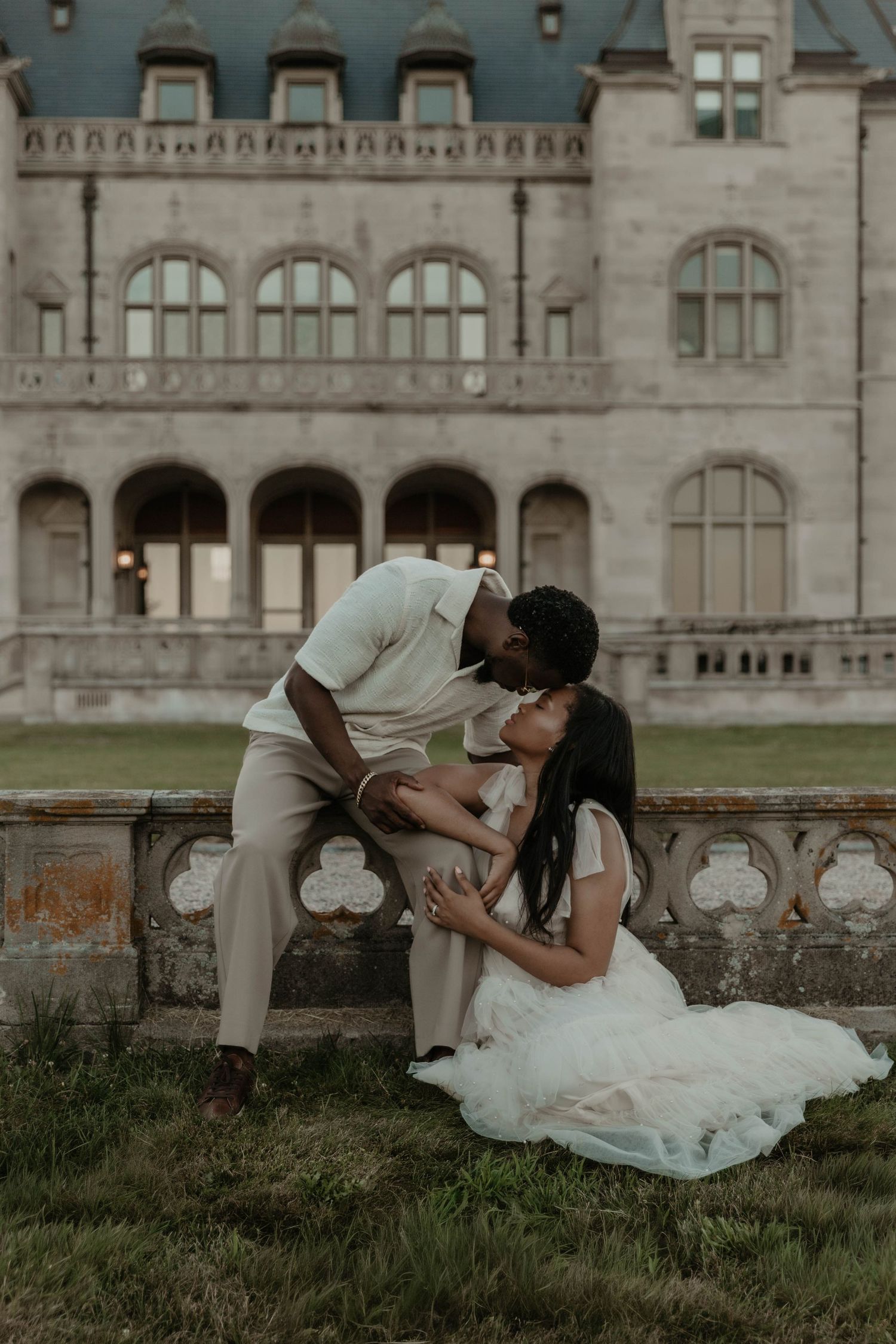 Couple sharing a romantic kiss in front of a grand historic mansion during an elegant outdoor engagement session.