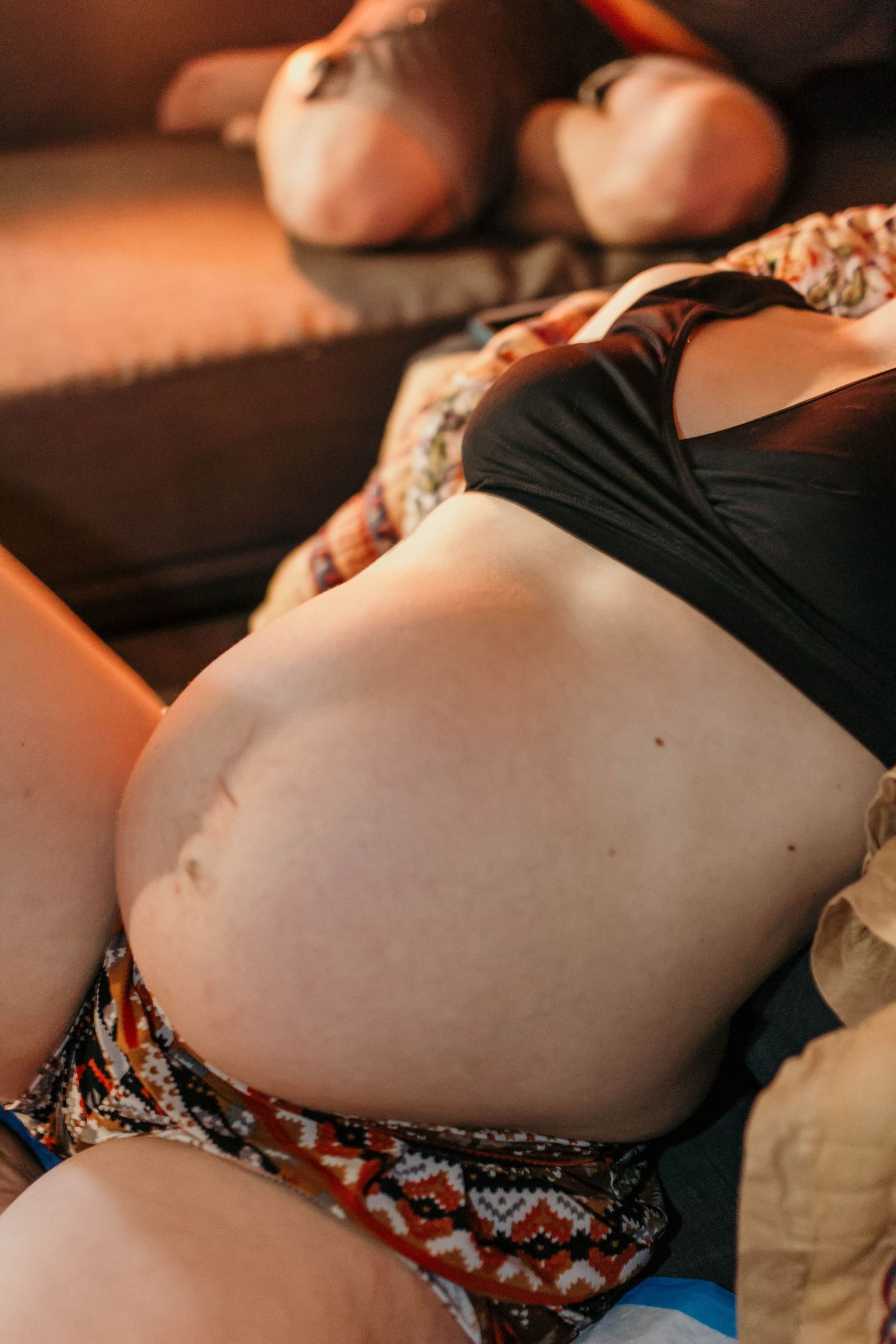 Close-up of a pregnant woman's bare baby bump while reclining on a couch in warm light.