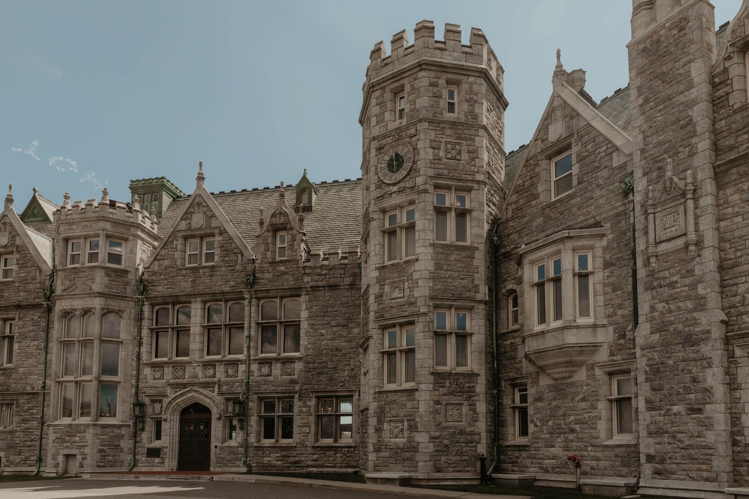 Historic stone castle with Gothic architecture, battlements, and a round tower under a cloudy sky.