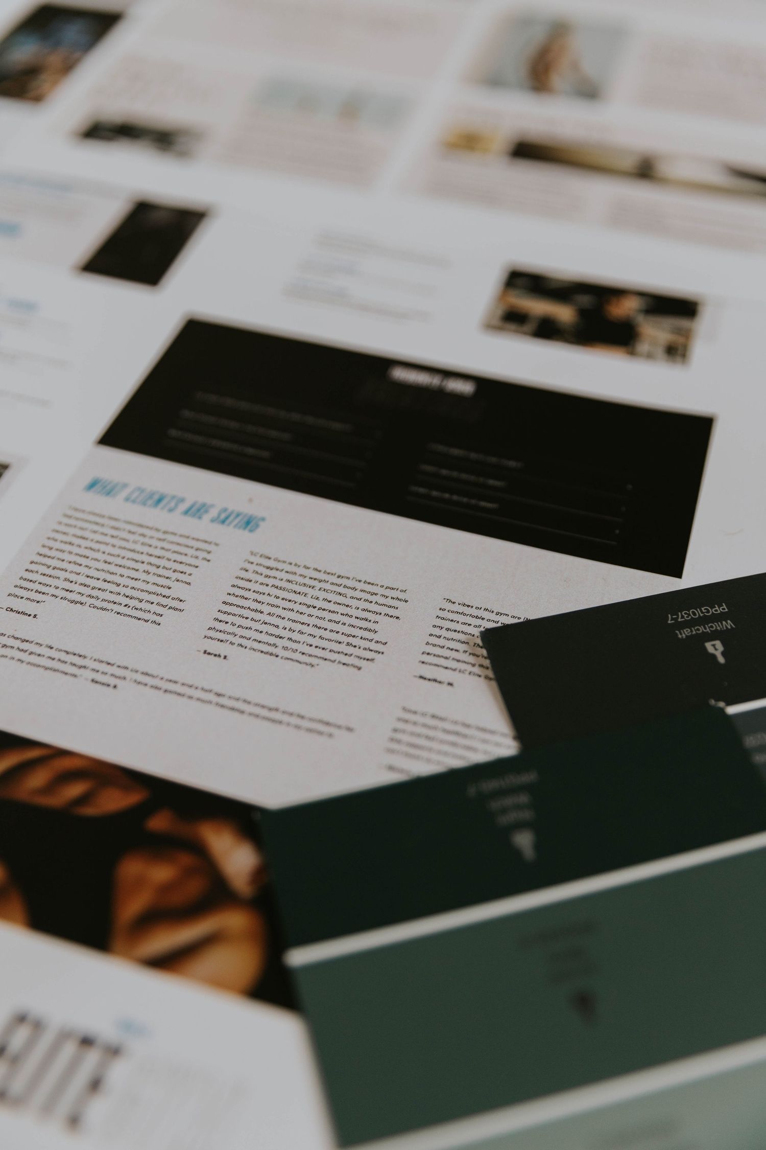 Flat lay of printed design documents and dark green business cards spread across a white surface.