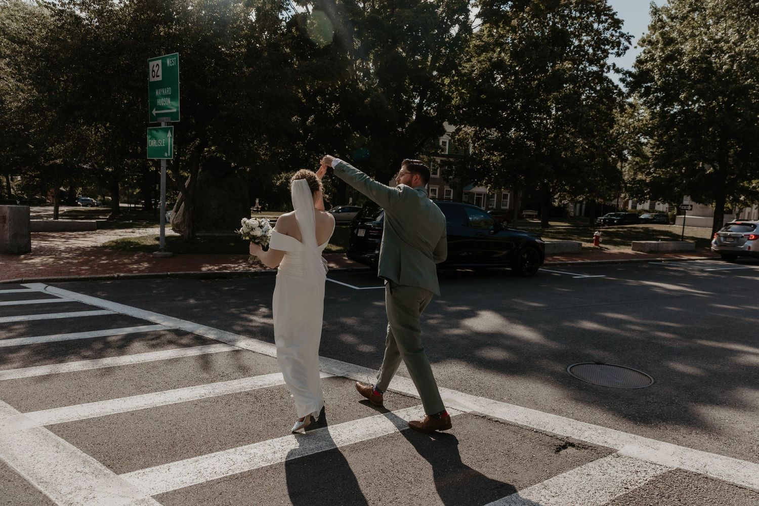 Bride and groom dancing in a crosswalk surrounded by trees on a sunny wedding day.