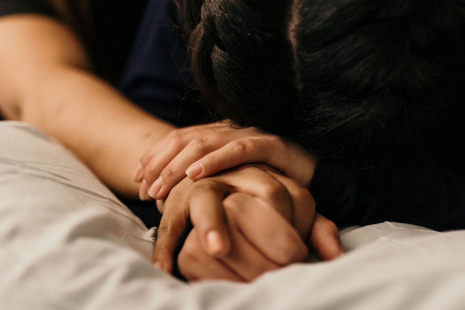 Two people holding hands tenderly on a white bed, symbolizing love, comfort, and emotional connection.
