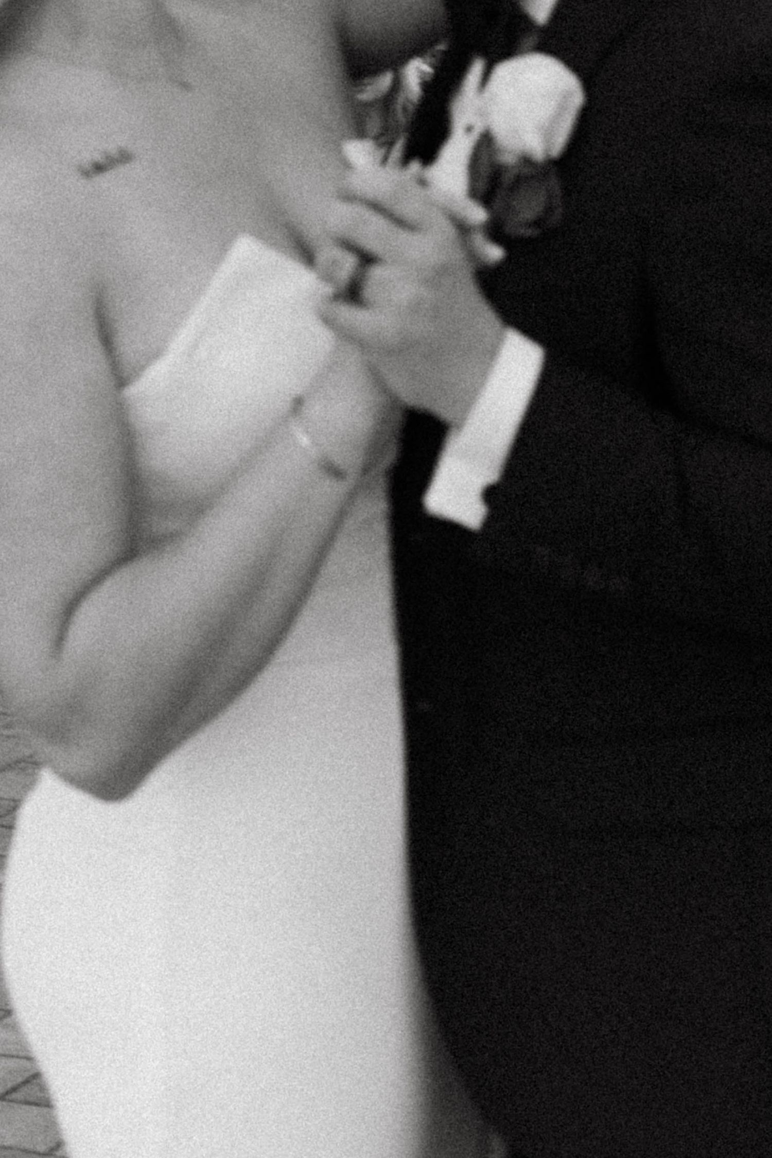 Black and white close-up of a bride in a strapless gown holding hands with a groom in a tuxedo with a boutonniere.