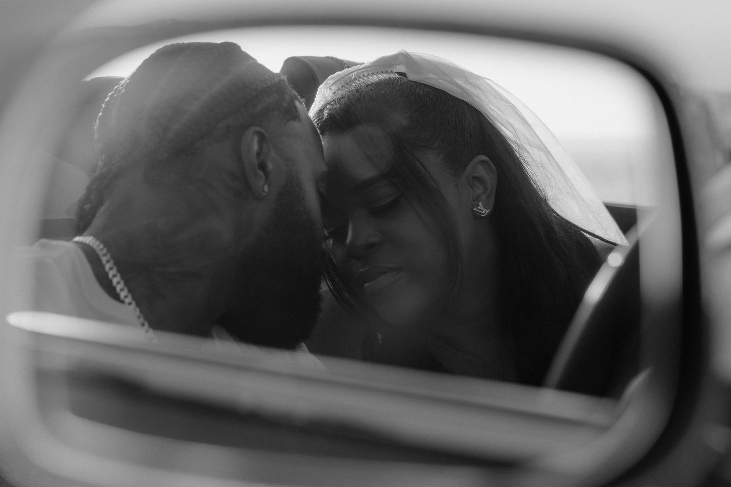 Black and white photo of a romantic couple sharing an intimate moment, reflected in a car mirror.