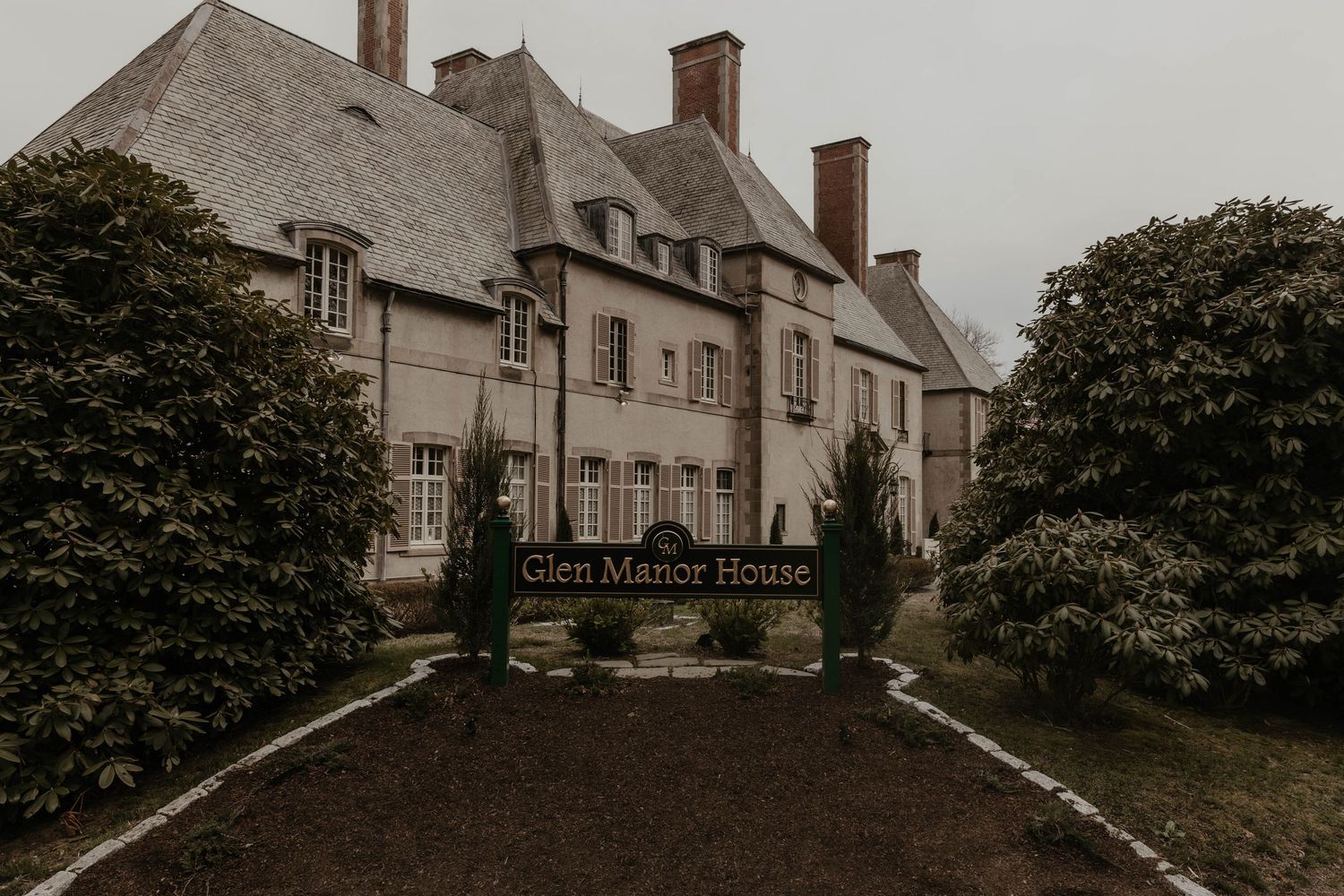 Glen Manor House exterior view showing elegant stone mansion with manicured hedges and formal entrance sign on overcast day.