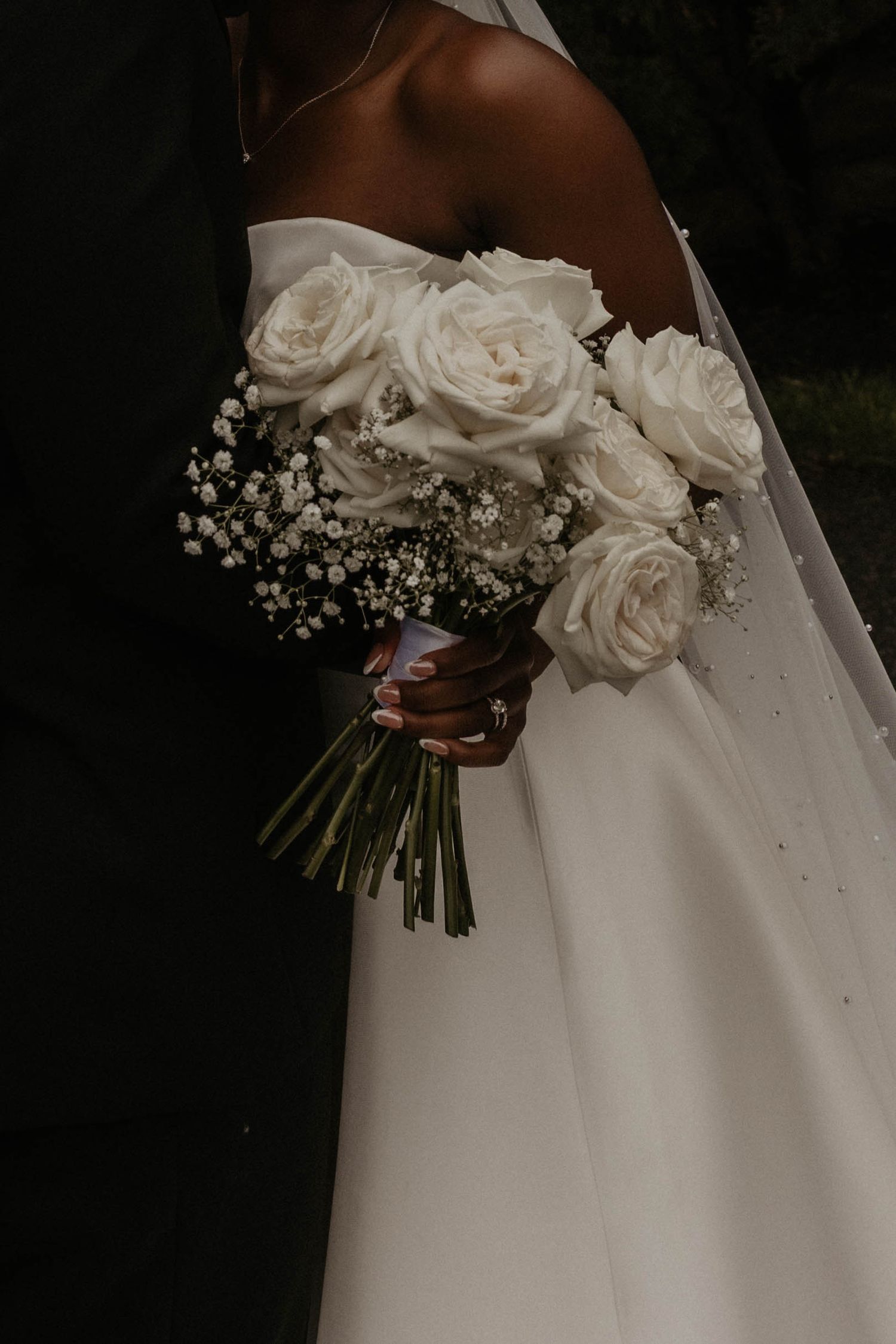 Close-up of bride holding lush white rose and baby's breath wedding bouquet against her strapless bridal gown.