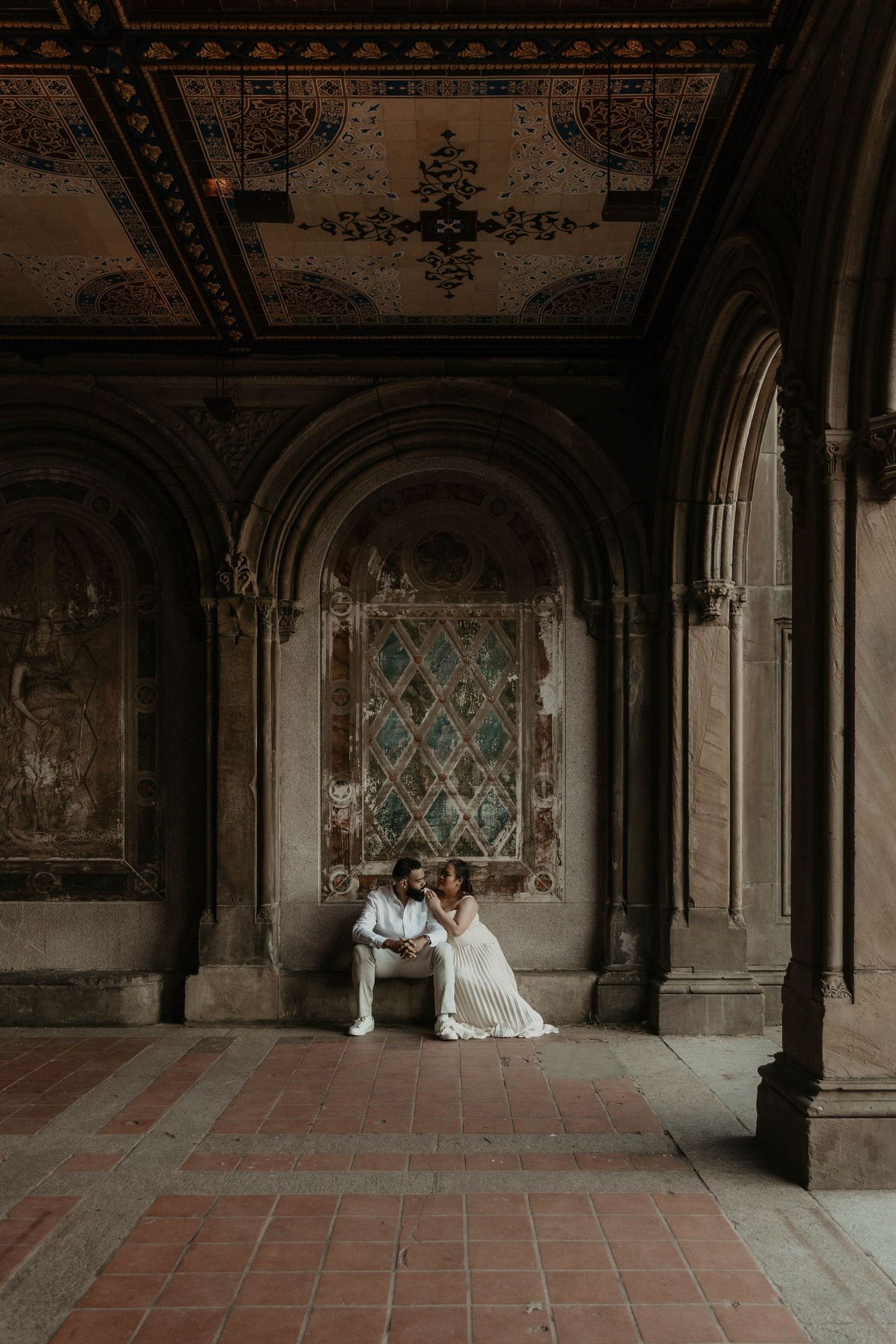 Couple in wedding attire sitting together under ornate arched ceiling at Bethesda Terrace, Central Park, NYC.