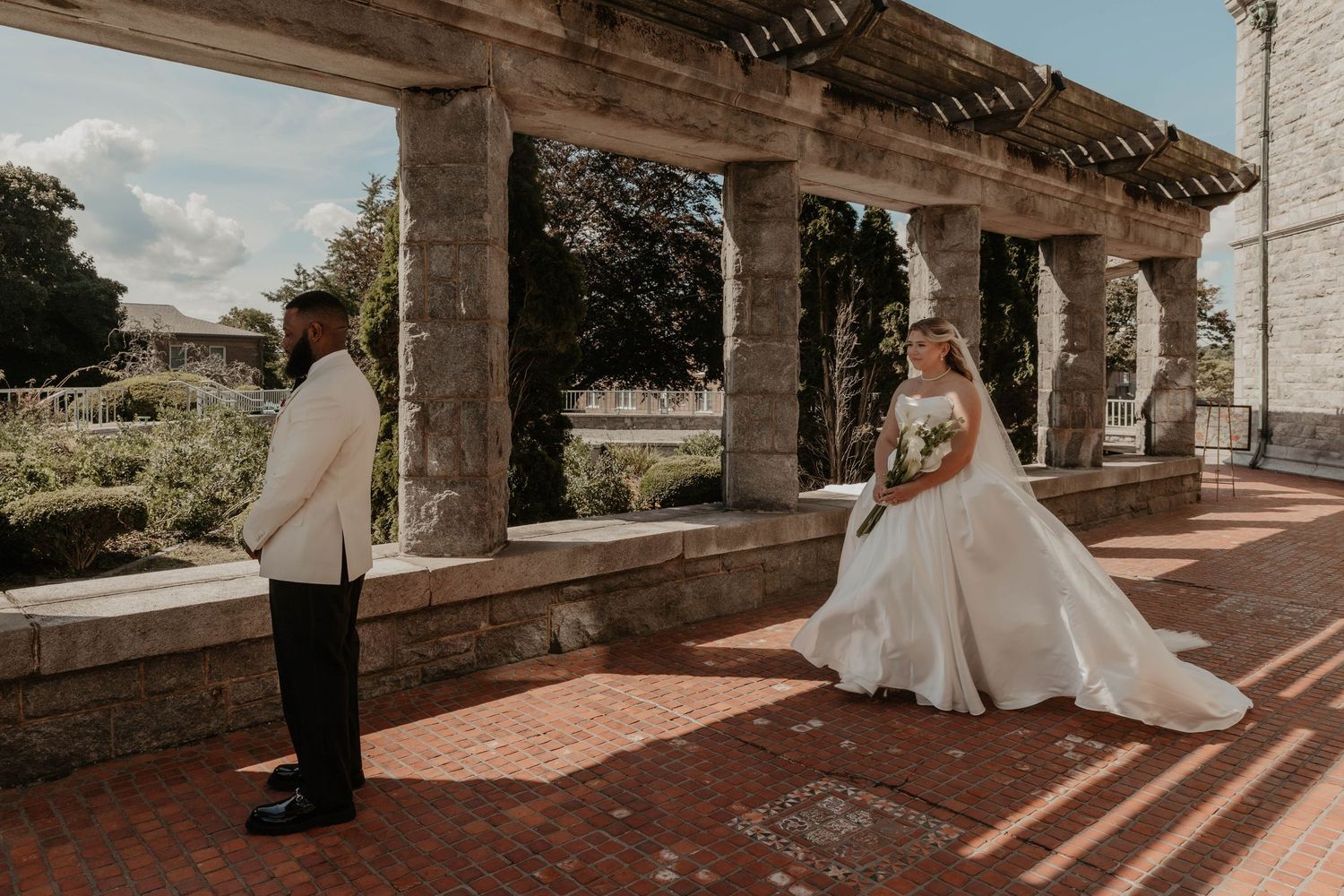 Bride and groom share a first look moment on a brick terrace with stone columns at an elegant outdoor wedding venue.
