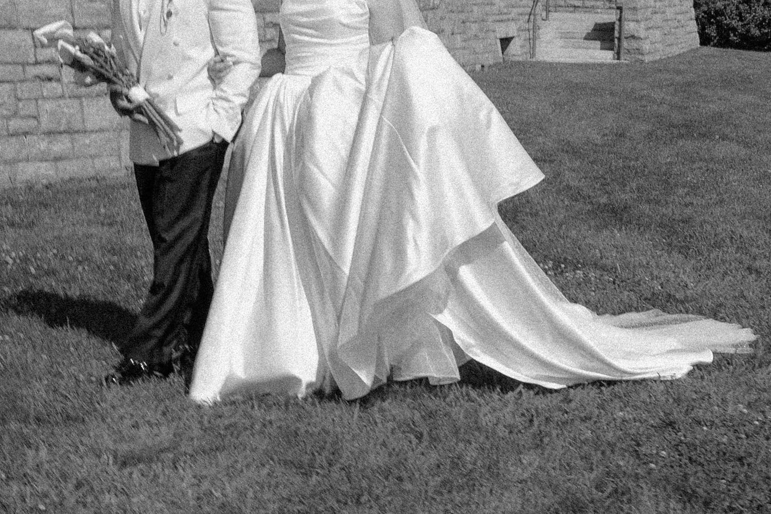 Black and white photo of bride and groom standing on grass showcasing wedding dress train.