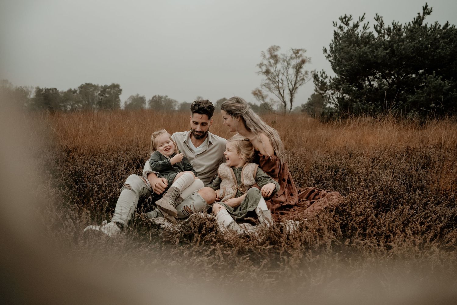 Een gezin zit samen in een rustiek, goudkleurig veld, gekleed in bijpassende witte outfits bij zonsondergang.