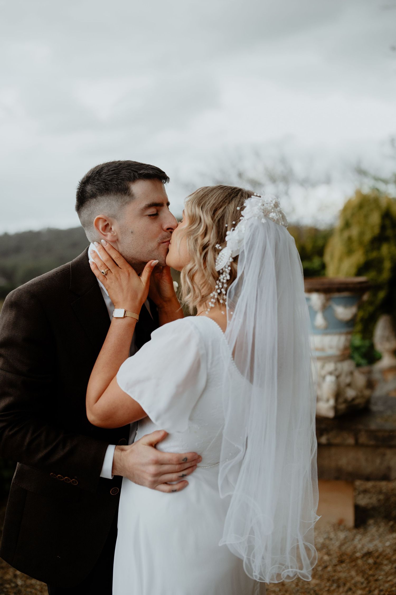 Intimate wedding kiss between bride and groom with countryside backdrop