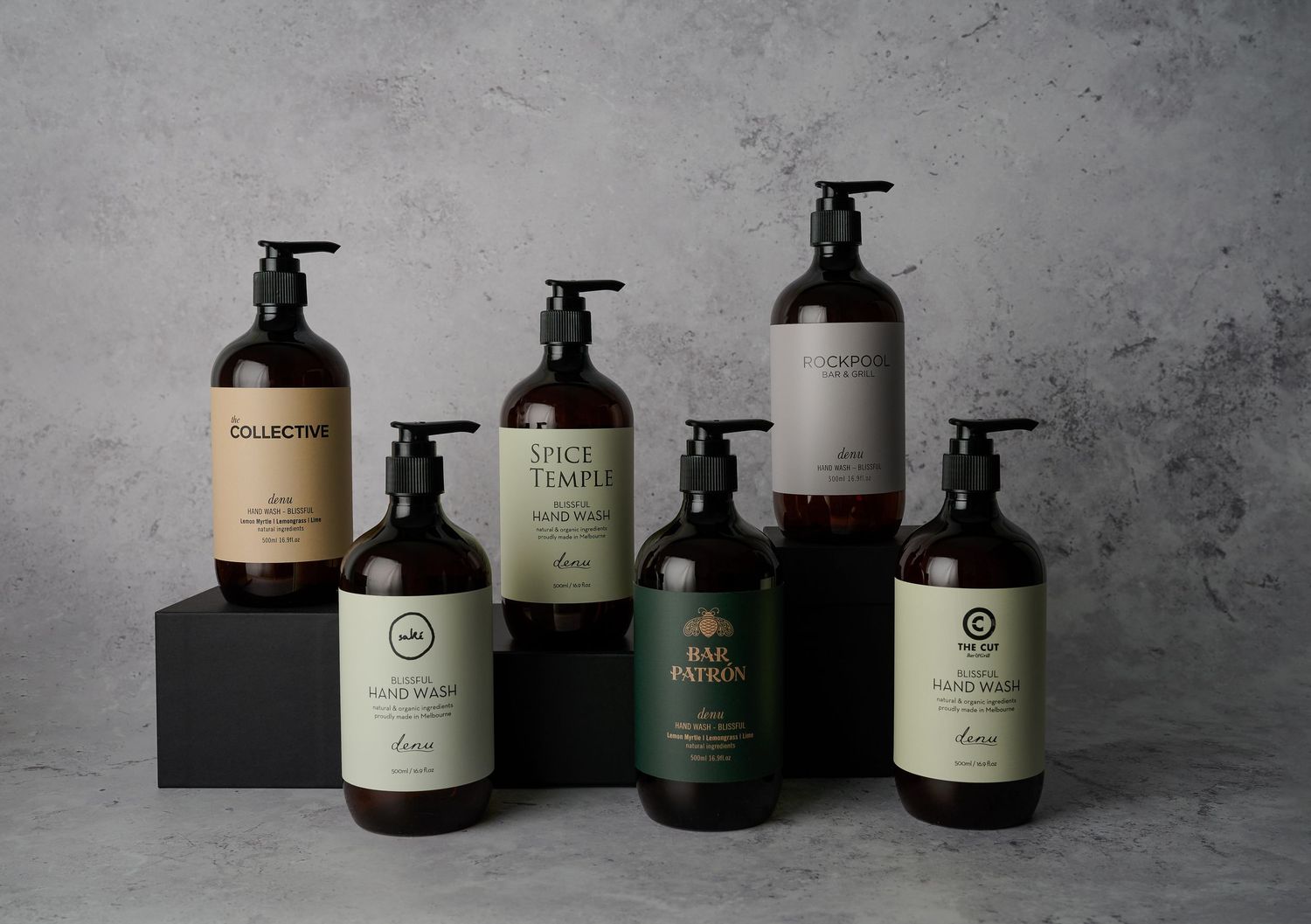 Collection of premium hand wash bottles including Collective, Spice Temple, Bar Patron and Rockpool brands arranged on concrete surface