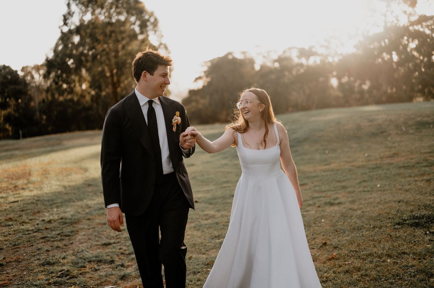 Romantic wedding couple walking hand in hand during golden hour countryside