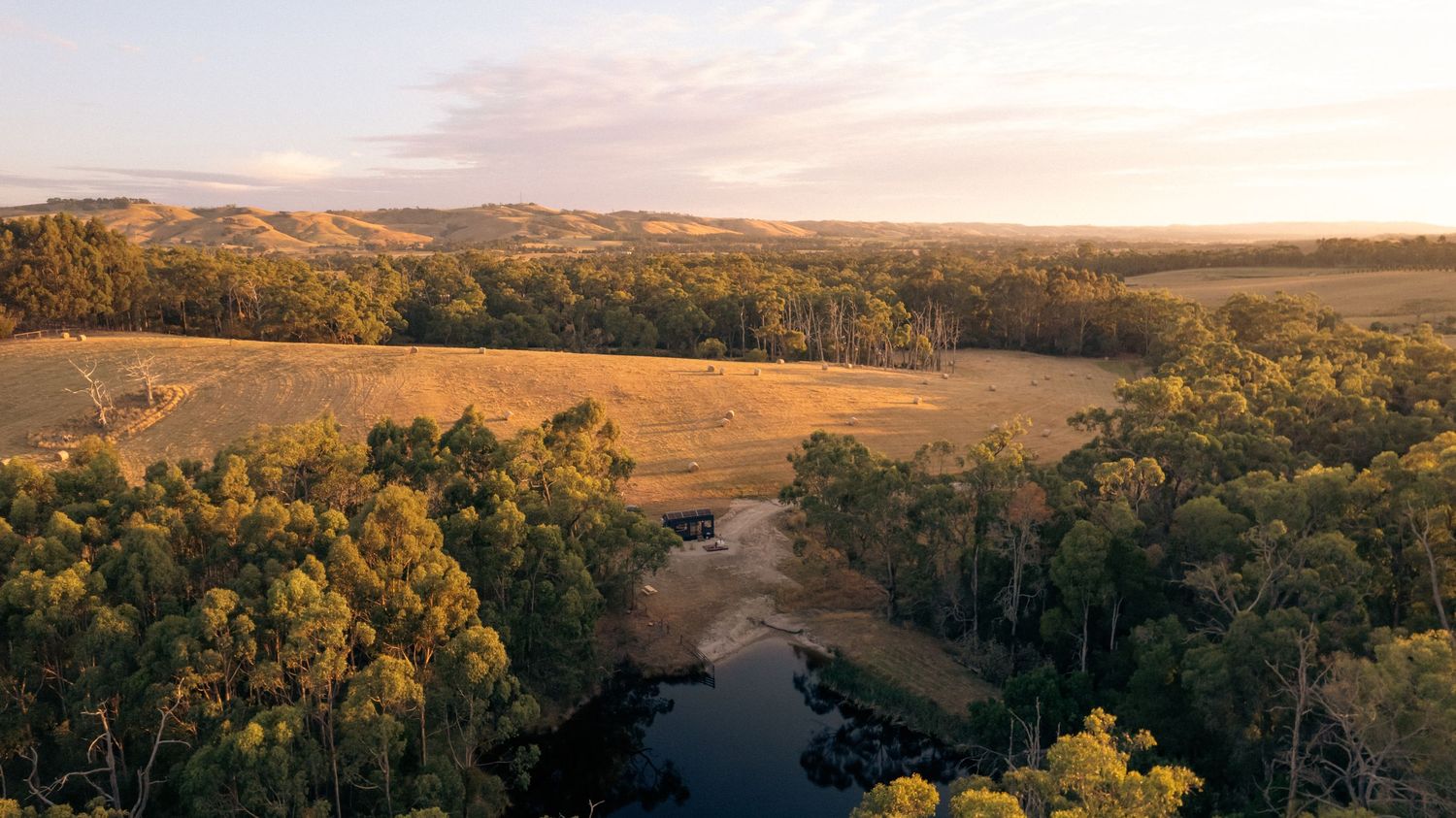 Aerial sunset view over golden farmland and winding country road in Victoria