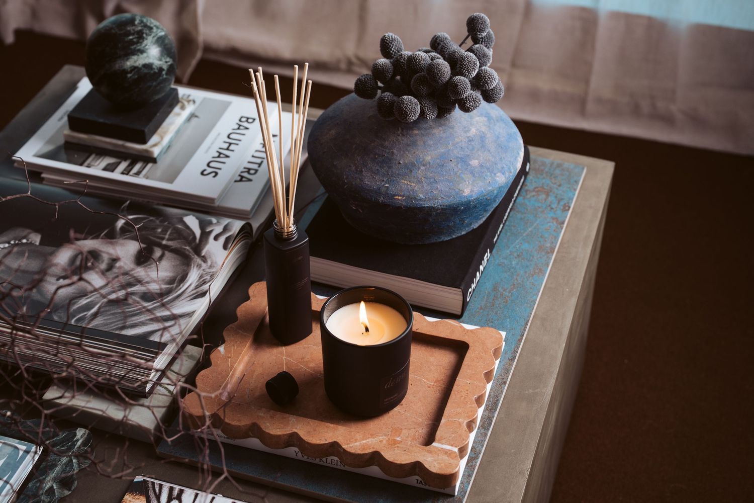 Styled lifestyle product photography featuring ceramic vase with dried flowers, reed diffuser, candle and Bauhaus magazine on wooden surface
