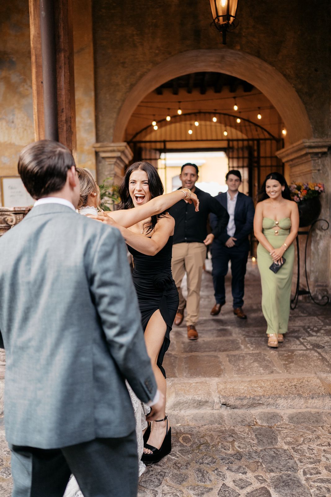 Guests arriving at an elegant outdoor wedding venue with string lights and stone archway.