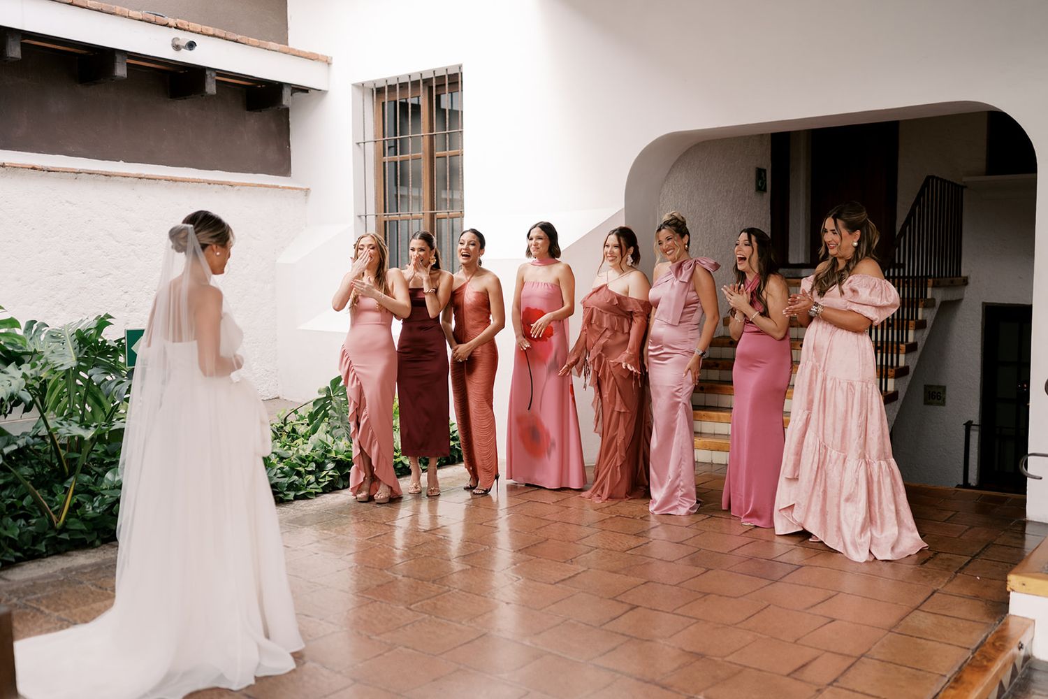 Bride in white gown reveals look to bridesmaids in pink and mauve dresses during wedding first look.