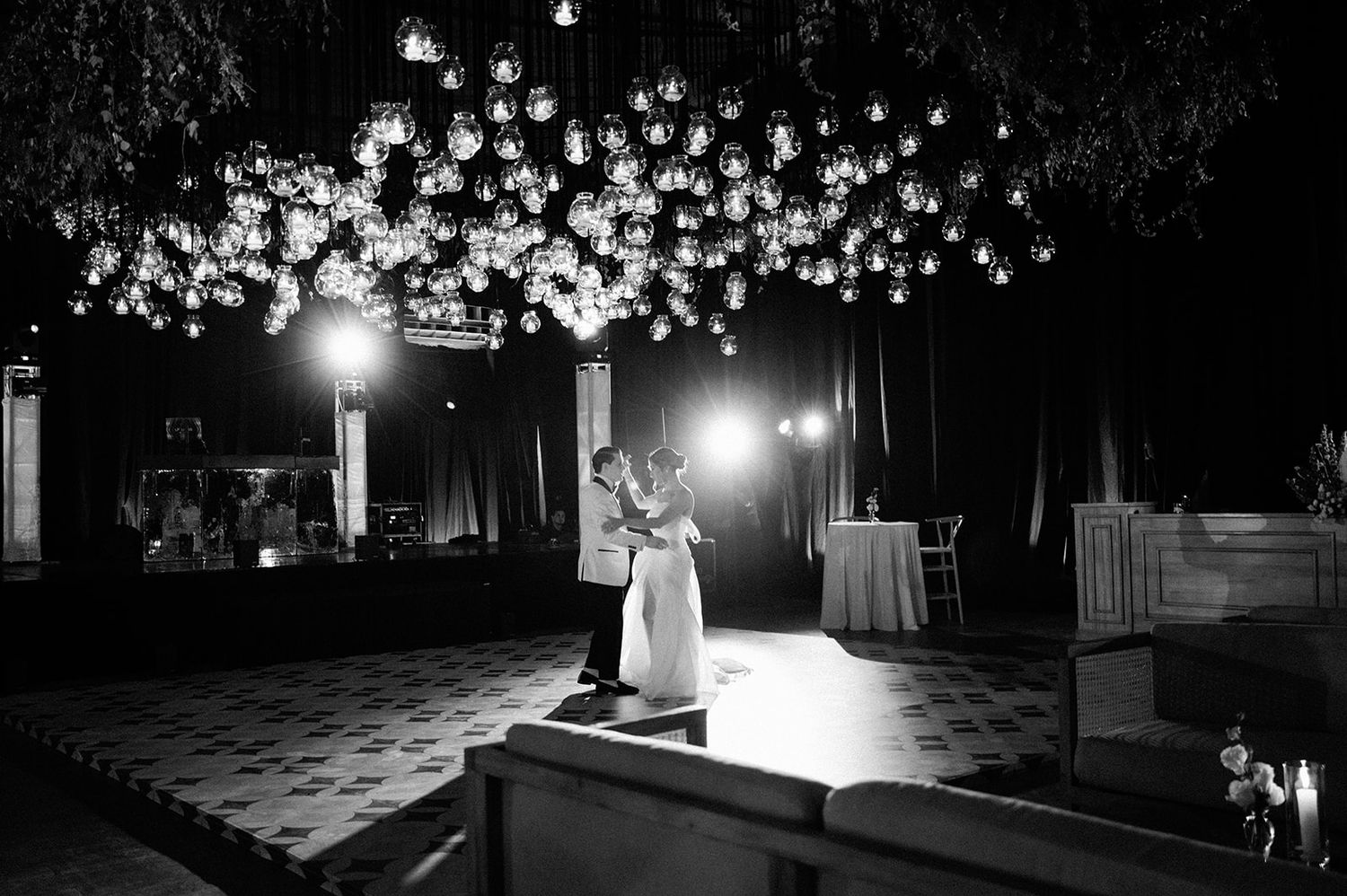 Couple shares first dance under glowing globe lights in elegant black and white wedding reception photo.