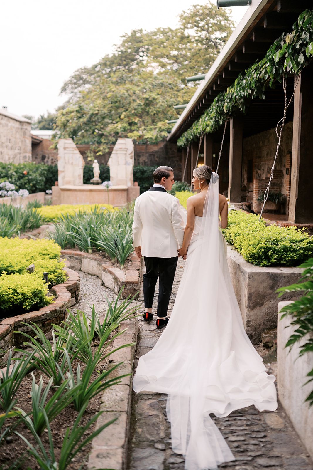 Bride and groom walk hand in hand through a lush garden courtyard at Casa Santo Domingo Antigua Guatemala